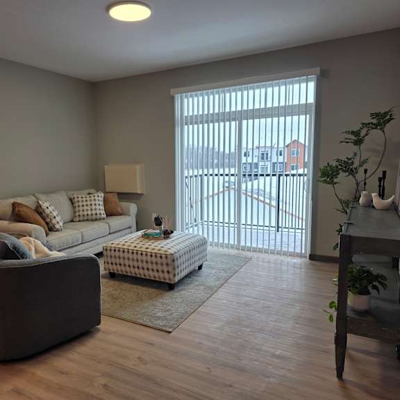 a living room with a grey couch, a white ottoman, and a wooden floor.