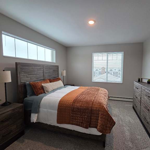 a bedroom with a large bed, a nightstand with a lamp, and a dresser with a mirror.