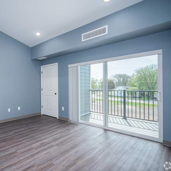 an empty living room with a large window and a door to a balcony