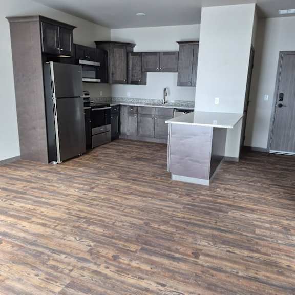 a kitchen with a black refrigerator and wooden floors.