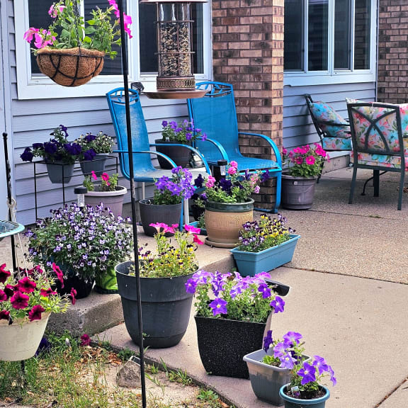 a front porch with pots of flowers and chairs on it