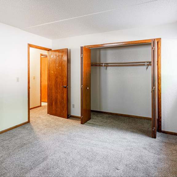 a room with a carpeted floor, a white wall, a window, and a wooden door.