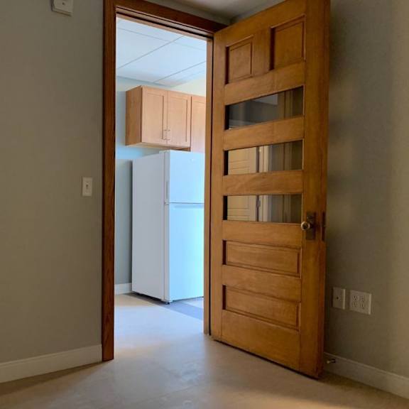 an empty room with a wooden door and a white refrigerator