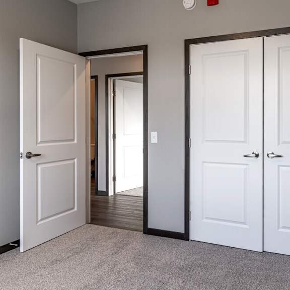 an empty room with white doors and a door to a hallway