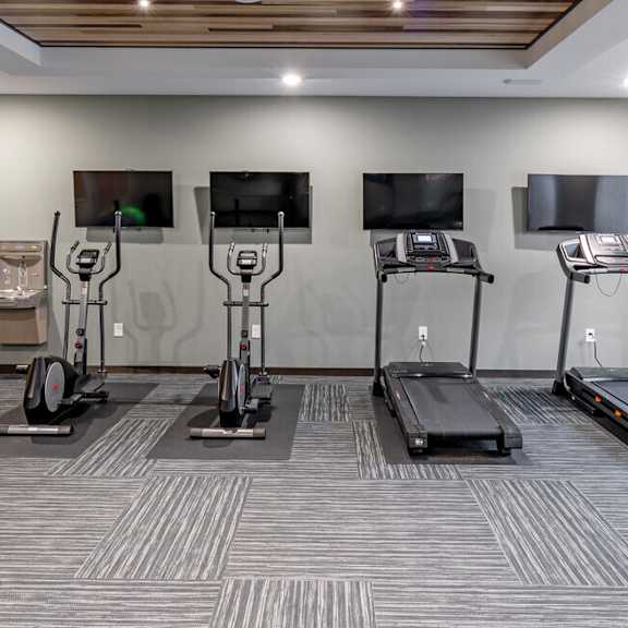 a gym with treadmills and televisions on the wall