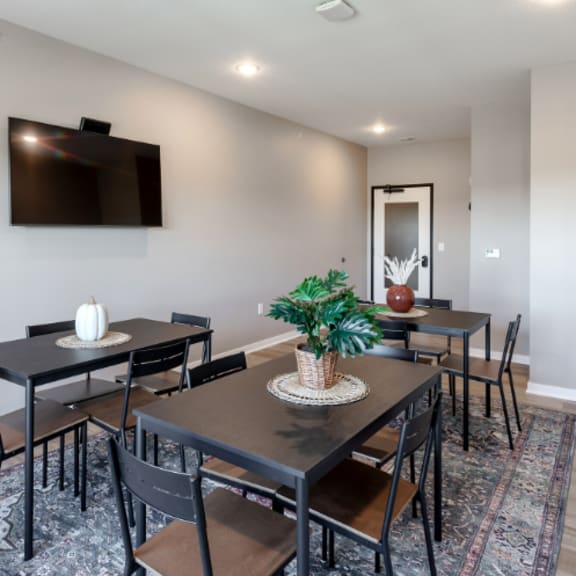 a black table with a vase and a basket on it is surrounded by chairs in a room with a flat screen tv mounted on the wall.