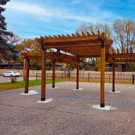 a wooden pergola structure in the middle of a paved area.