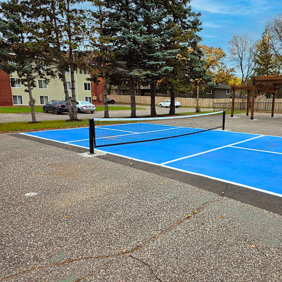 a blue tennis court surrounded by trees and a fence.