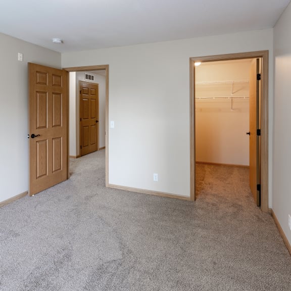an empty living room with two doors and a hallway to a bedroom
