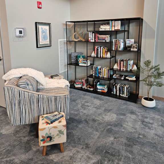 a room with a bookshelf, a chair, and a small tree.