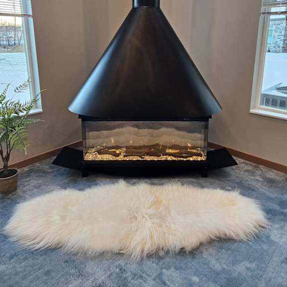 a black wood stove in a room with a white furry rug in front of it.