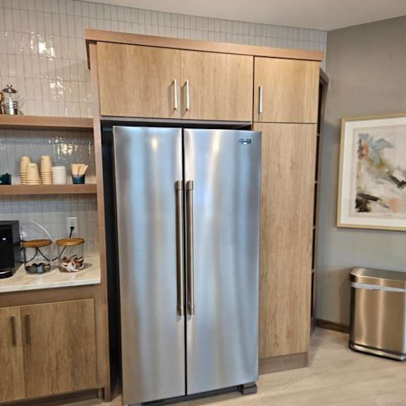 a stainless steel refrigerator with wooden cabinets and a trash can in a kitchen.