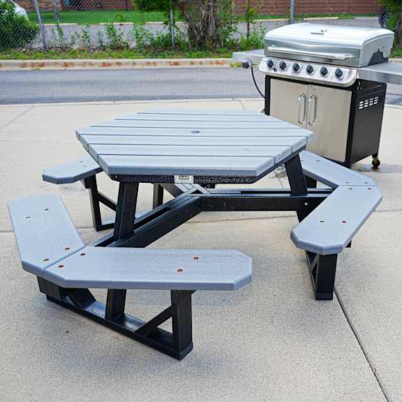 a picnic table with two benches is in the foreground with a grill and trash can in the background.