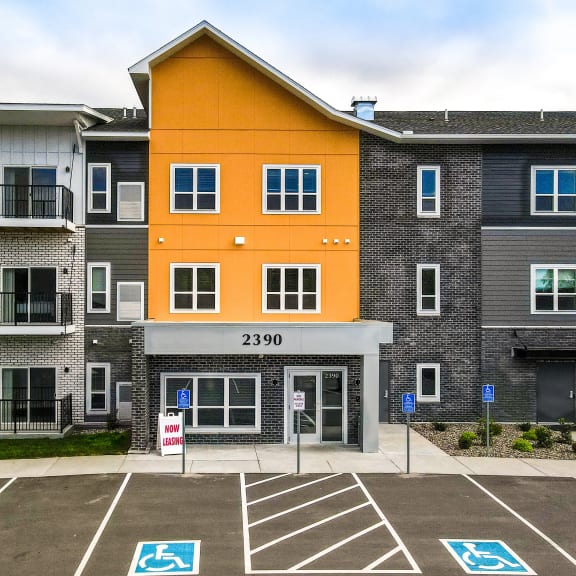 an apartment building with an orange and gray facade in a parking lot