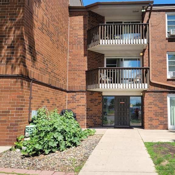 a brick building with a balcony and a small garden in front.