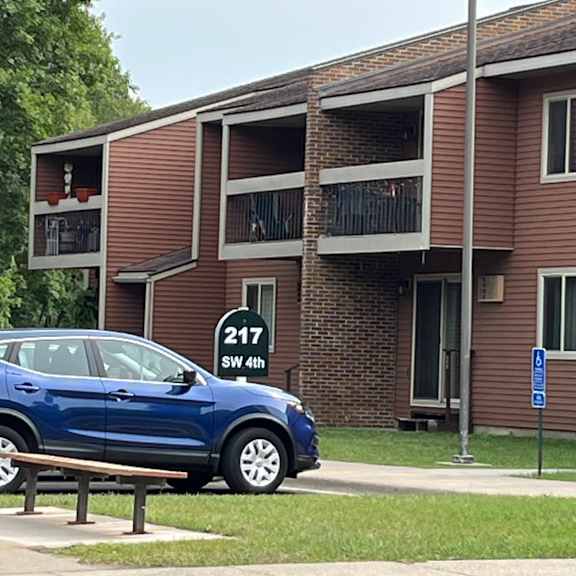 a blue car is parked on the side of a road in front of a brown building.