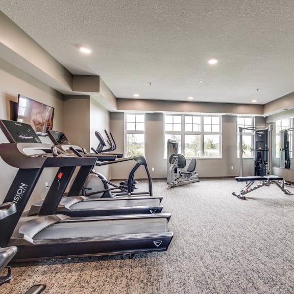 a gym with treadmills and other exercise equipment in a room with windows