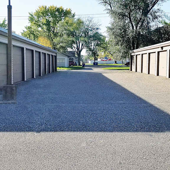 a long driveway with a brick wall on the left and a row of garage doors on the right.