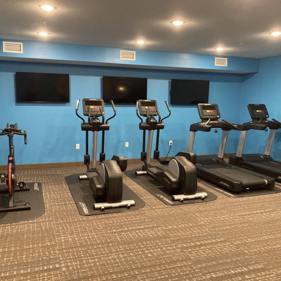 a row of exercise bikes in a gym with televisions
