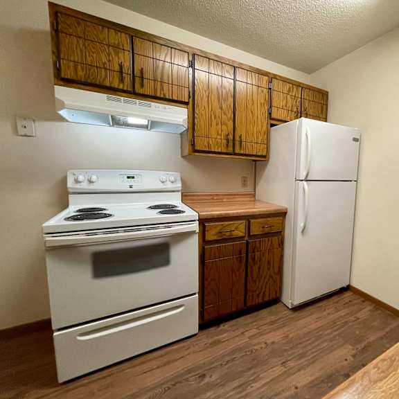 a kitchen with a white stove and refrigerator, wooden cabinets, and a sink.