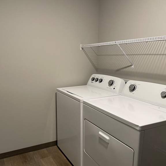 a laundry room with a washer and dryer and a shelf on the wall