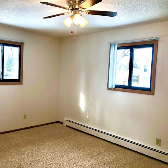 a room with a ceiling fan and two windows.