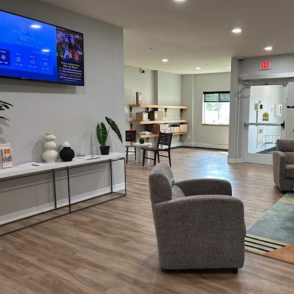 a waiting room with grey chairs and a television on the wall.