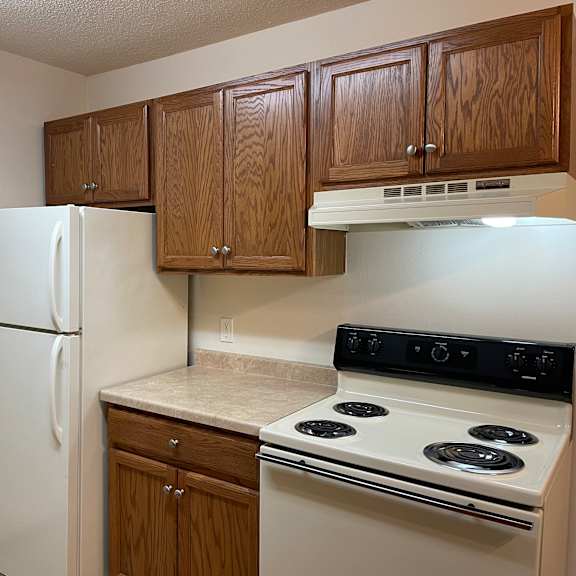 a kitchen with a white refrigerator, wooden cabinets, and a white stove top oven.