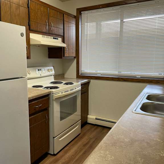 a kitchen with a white refrigerator, white oven, and a window with blinds.