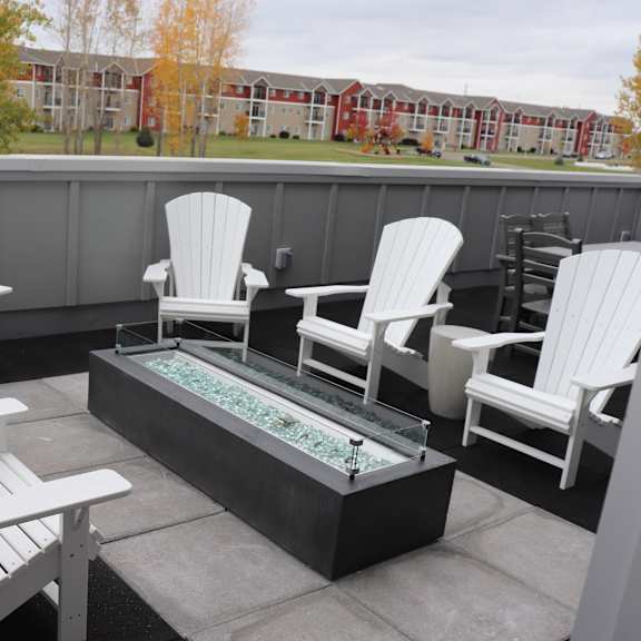 a group of white chairs around a fire pit on a rooftop patio