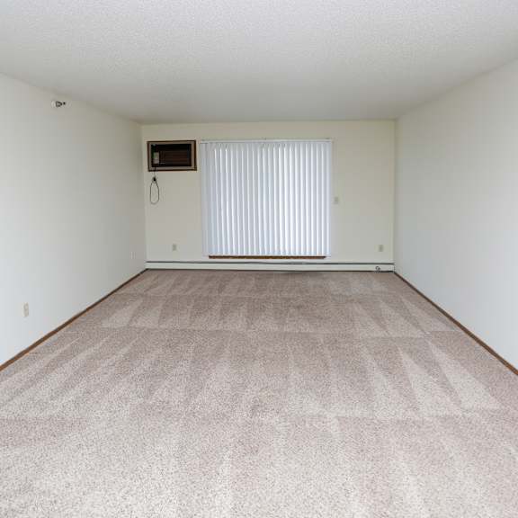 the living room and dining room of an apartment with white walls and carpeting