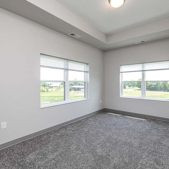 a large empty room with two windows and carpeted floor.