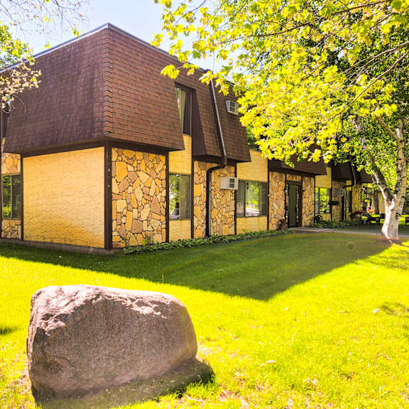 a large rock sits in the foreground of a building with a brown roof and yellow walls.
