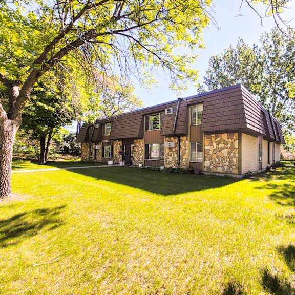 a house with a brown roof is surrounded by green grass and trees.
