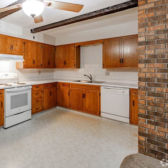 a kitchen with a white refrigerator, wooden cabinets, and a brick wall.