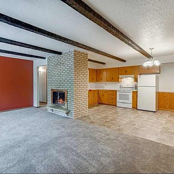 a living room with a fireplace and a kitchen area in the background.