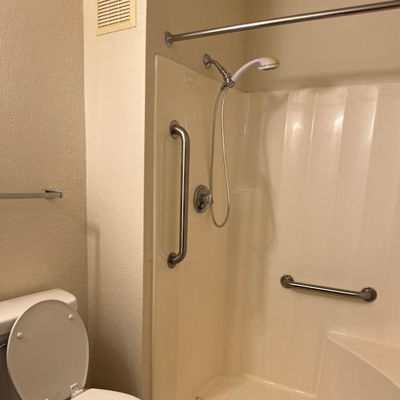 a white toilet with a closed lid is in a bathroom with a white tub and silver grab bars.