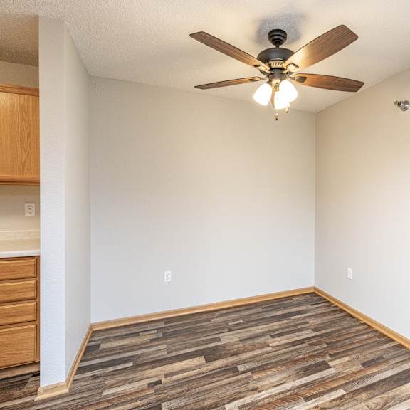 a room with a ceiling fan and wooden flooring.