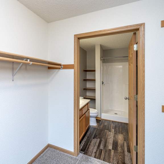 a white wall with a wooden shelf and a doorway leading to a bathroom.