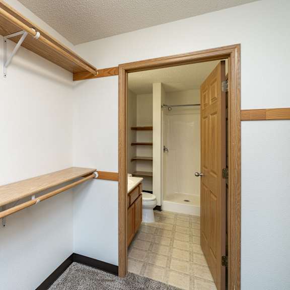 a white wall with a brown shelf and a doorway leading to a bathroom.
