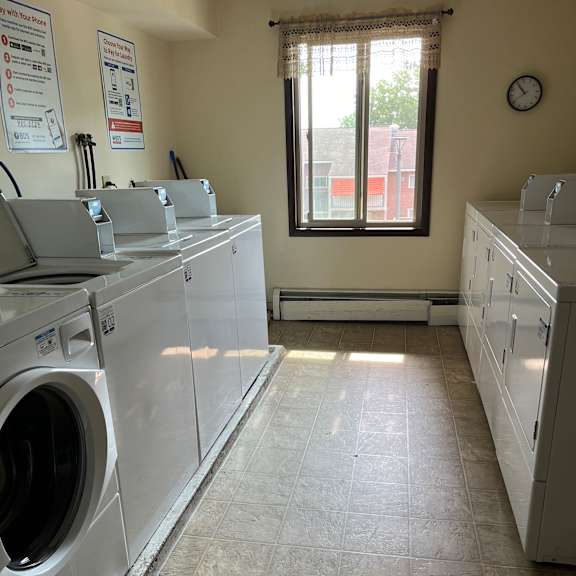 a washing machine is in a room with a window and a clock on the wall.