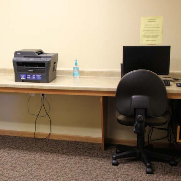 two chairs sit at a desk with a monitor, keyboard, and a printer.
