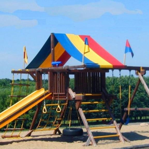 a playground with a yellow slide and a wooden structure with flags.