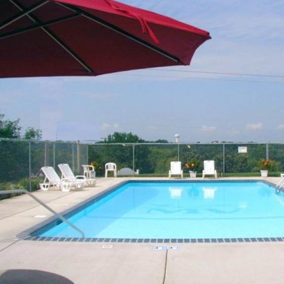 a red umbrella is shading a pool area with chairs.