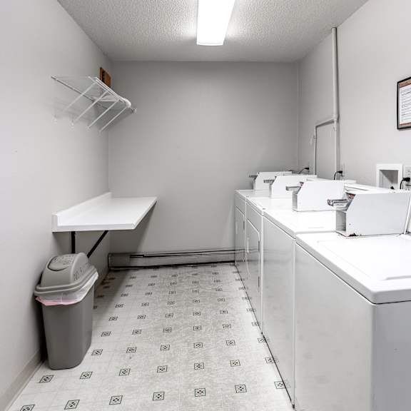 a laundry room with a washer and dryer, a trash can, and a white counter.