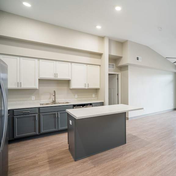 an empty living room with a kitchen and a ceiling fan