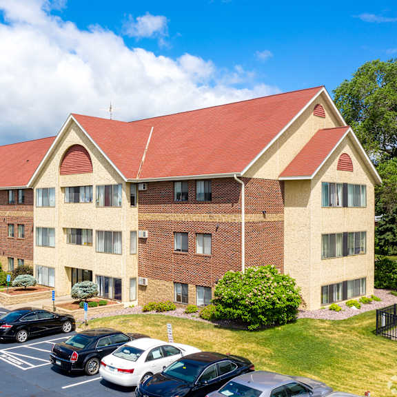 a large apartment building with a red roof and cars parked in front.