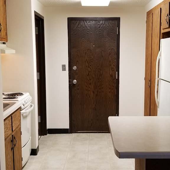a kitchen with a white counter top and a brown door.