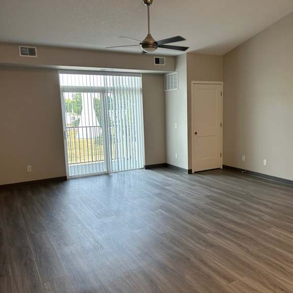 an empty living room with a sliding glass door and a ceiling fan