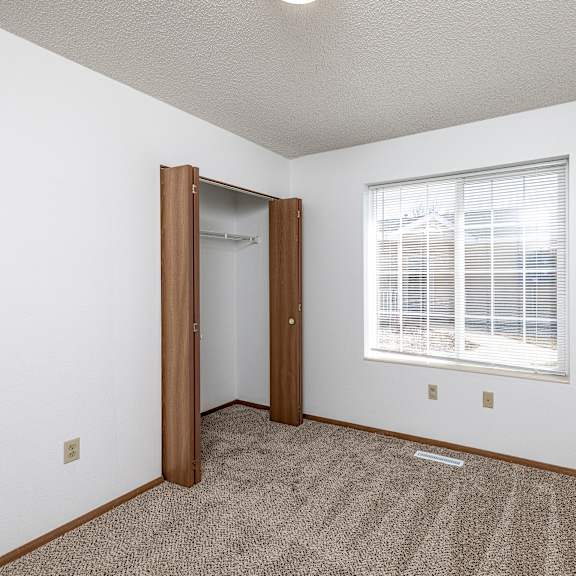 a room with a carpeted floor, a window with blinds, and a door.